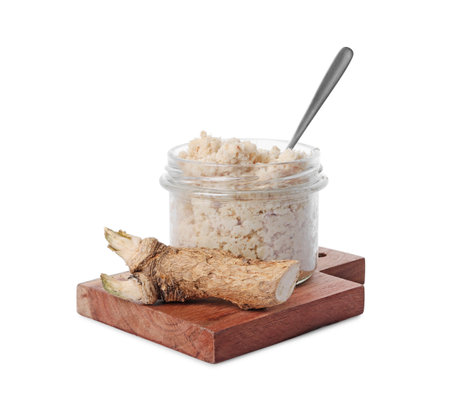 Wooden board with glass jar of tasty prepared horseradish, spoon and root isolated on whiteの写真素材