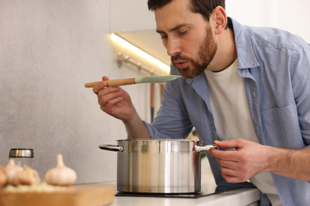 Man tasting delicious chicken soup in kitchenの写真素材