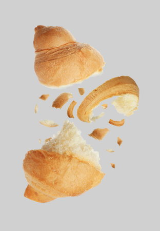 Pieces of delicious fresh croissant falling on gray background