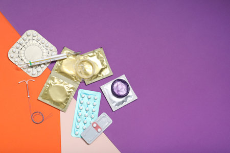 Contraceptive pills, condoms, intrauterine device and thermometer on color background, flat lay with space for text. Choice of birth control methodの写真素材