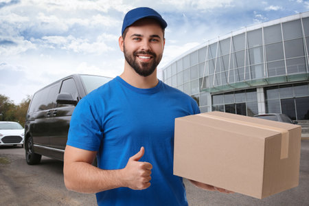 Happy courier with parcel showing thumbs up outdoorsの写真素材