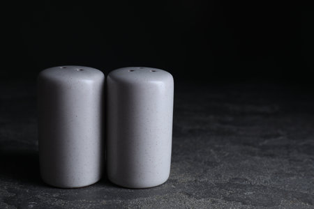 Salt and pepper shakers on dark textured table. Space for textの写真素材