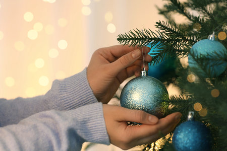 Woman decorating Christmas tree with light blue festive ball on blurred background, closeupの写真素材