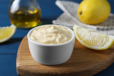 Tasty mayonnaise in bowl and lemon wedge on blue table, closeupの写真素材