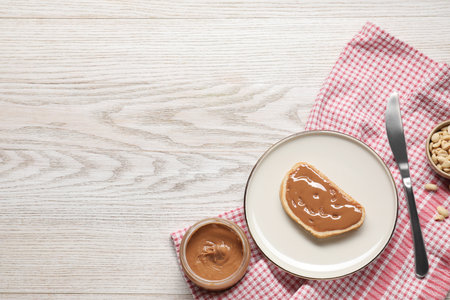 Toast with tasty nut butter and knife on white wooden table, flat lay. Space for text