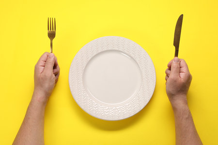 Man with fork, knife and empty plate at yellow table, top viewの写真素材
