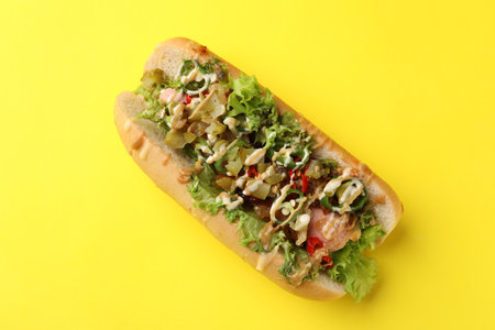 Delicious hot dog with chili peppers, lettuce, pickles and sauces on yellow background, top viewの写真素材