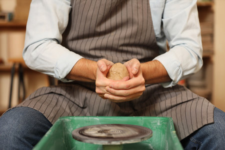 Man crafting with clay over potter's wheel indoors, closeupの写真素材