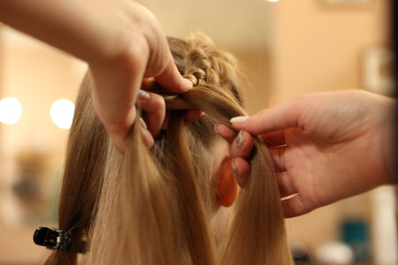 Professional hairdresser braiding girl's hair in beauty salon, closeup