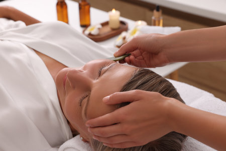 Woman receiving facial massage with jade gua sha tool in beauty salon, closeupの写真素材