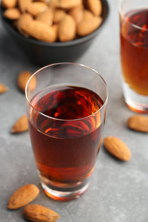 Glass with tasty amaretto liqueur and almonds on gray table, closeup