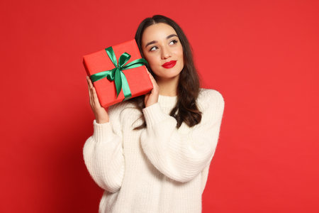 Beautiful young woman with Christmas gift on red backgroundの写真素材