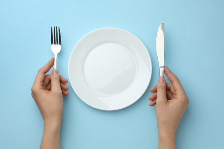 Woman with fork, knife and clean plate at light blue table, top viewの写真素材