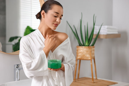 Young woman applying aloe gel onto her skin in bathroom. Space for textの写真素材