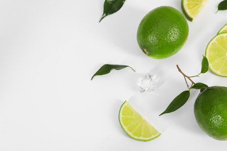 Flat lay composition with fresh limes, leaves and ice cube on white background. Space for textの写真素材