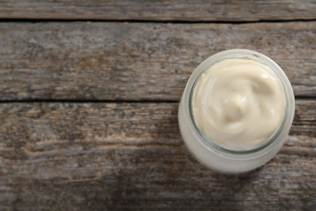 Fresh mayonnaise sauce in glass jar on wooden table, top view. Space for textの写真素材