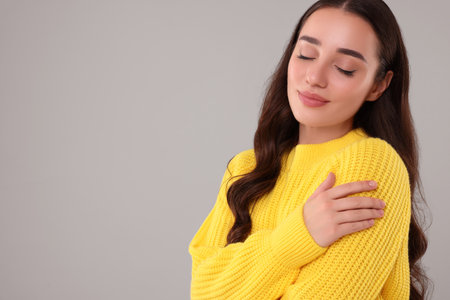 Beautiful young woman in stylish warm sweater on gray background, space for textの写真素材