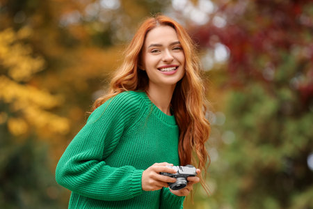 Smiling woman with camera in autumn parkの写真素材