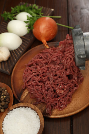 Meat grinder with beef mince, onion, parsley and spices on wooden tableの写真素材