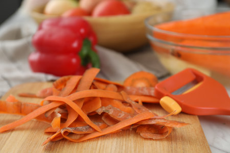 Wooden board with carrot peels and peeler on white table, closeupの写真素材
