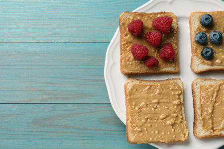 Delicious toasts with peanut butter, raspberries and blueberries on light blue wooden table, top view. Space for textの写真素材