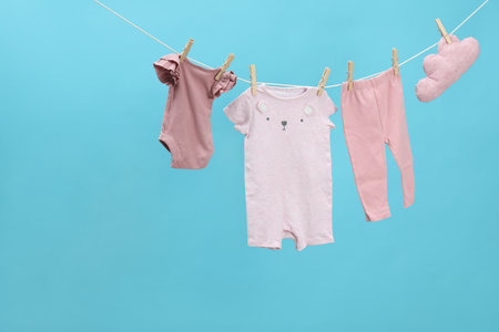 Different baby clothes and cloud shaped pillow drying on laundry line against light blue background. Space for textの写真素材
