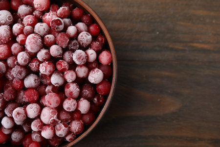 Frozen red cranberries in bowl on wooden table, top view. Space for textの写真素材