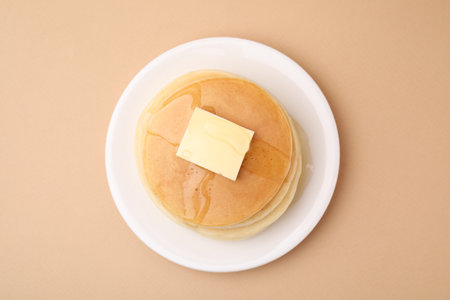 Delicious pancakes with butter and honey on beige background, top view