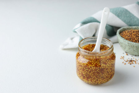 Whole grain mustard and spoon in jar on white table. Space for textの写真素材