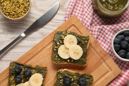 Toasts with tasty pistachio butter, banana slices, blueberries and nuts on white wooden table, flat...