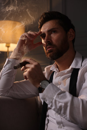 Handsome man smoking cigar at home in eveningの写真素材