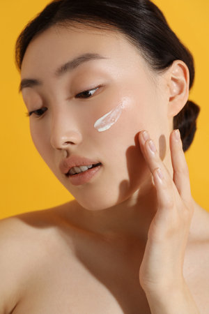 Beautiful young woman with sun protection cream on her face against orange backgroundの写真素材