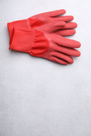 Pair of red gardening gloves on light gray table, above view. Space for text