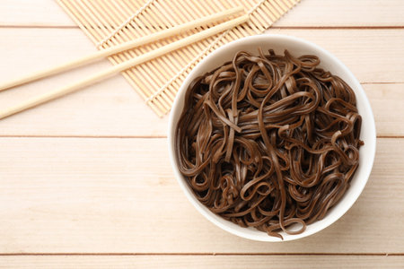 Tasty buckwheat noodles (soba) with chopsticks on wooden table, flat lay. Space for text