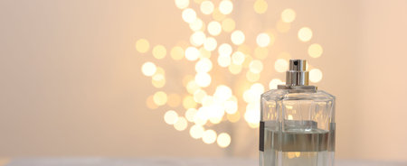 Bottle of perfume against beige background with blurred lights, space for textの写真素材