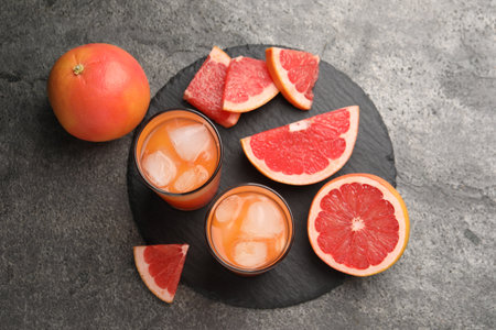 Tasty grapefruit drink with ice in glasses and fresh fruits on dark textured table, flat layの写真素材