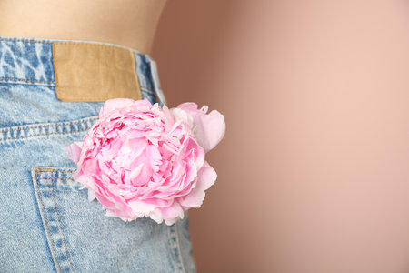Woman with pink peony in pocket on beige background, closeup. Space for textの写真素材