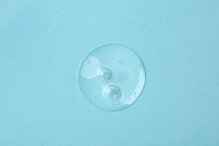Sample of cosmetic serum on light blue background, top view
