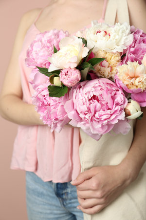 Woman with bouquet of beautiful peonies in bag on beige background, closeupの写真素材