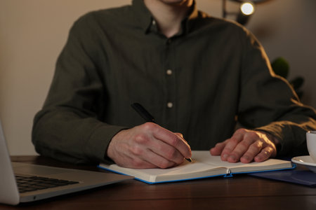 Man taking notes at wooden table indoors, closeupの写真素材