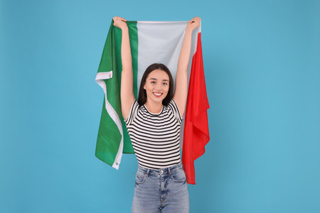 Young woman holding flag of Italy on light blue backgroundの写真素材