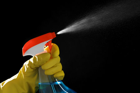 Woman spraying liquid from bottle on black background, closeupの写真素材