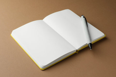Open notebook with blank pages and pen on light brown backgroundの写真素材