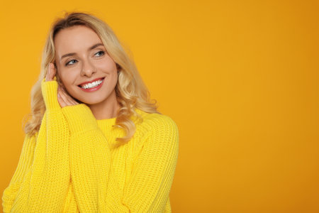 Happy woman in stylish warm sweater on orange background. Space for textの写真素材