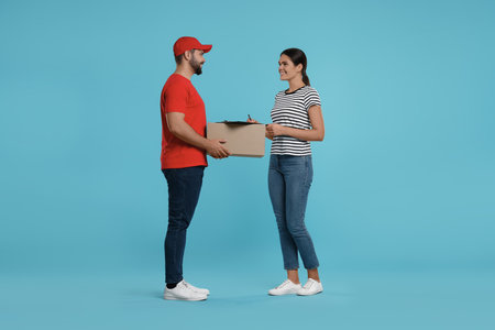 Smiling woman signing order receipt on light blue background. Courier deliveryの写真素材