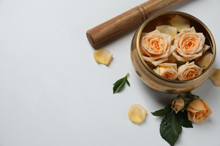 Tibetan singing bowl with water, mallet and beautiful rose flowers on white background, above view. Space for textの写真素材