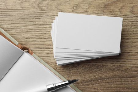 Stack of blank business cards, notebook and pen on wooden table, flat lay. Mockup for designの写真素材