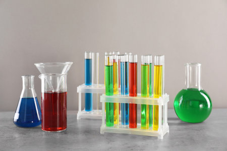 Test tubes with liquids in stand and flasks on table against light gray background