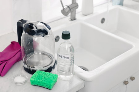 Cleaning electric kettle. Bottle of vinegar, sponge, rubber gloves and baking soda on countertop in kitchenの写真素材