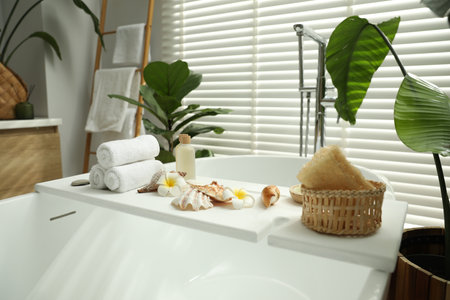 Bath tray with spa products, towels and shells on tub in bathroomの写真素材